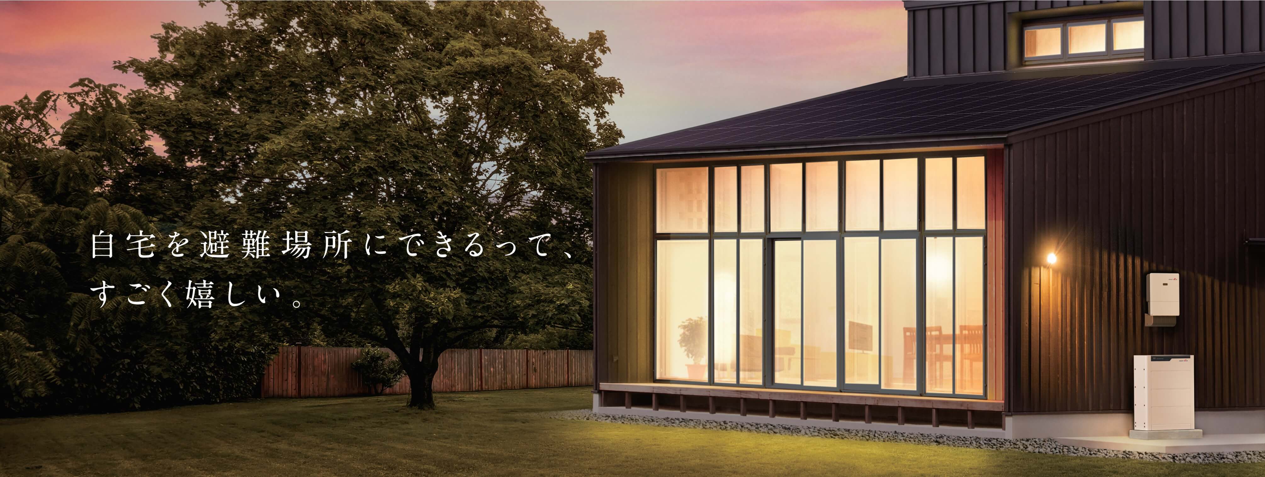 太陽光発電付き日本住宅の外壁に設置された蓄電池。夕景バナーに「自宅を避難場所にできるって、すごく嬉しい。」の文字入り。